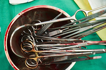 Blood-stained surgical instruments in a metal bowl on a green operating table