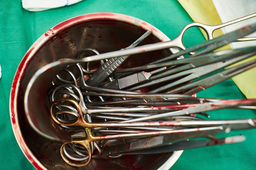 Blood-stained surgical instruments in a metal bowl on a green operating table