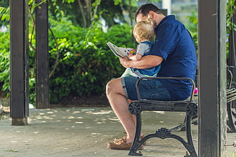 Father Reading Book to Toddler Daughter on Park Bench