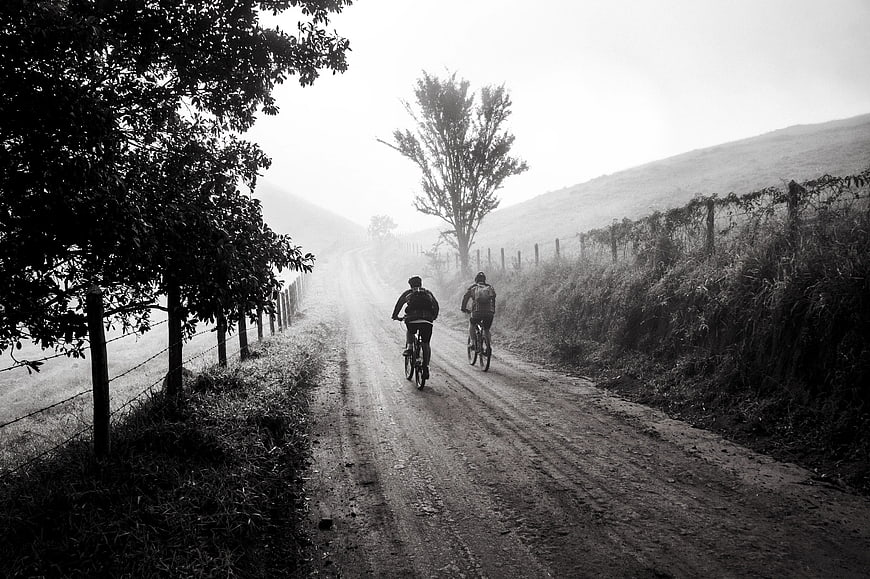 Two Cyclists Riding on Misty Rural Dirt Road
