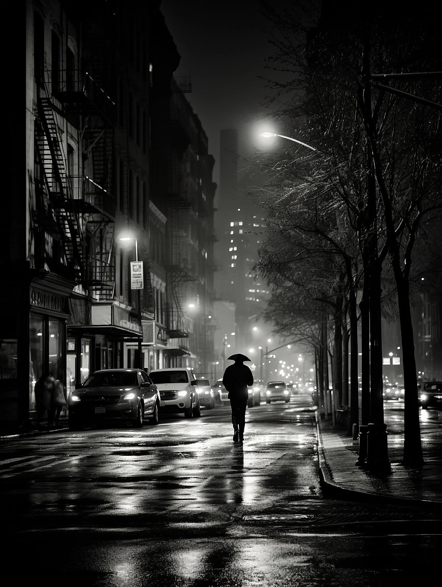 Silhouette of Person with Umbrella on Rainy City Street at Night