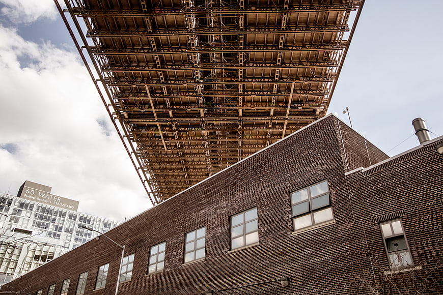 Low angle view of brick building under steel bridge structure