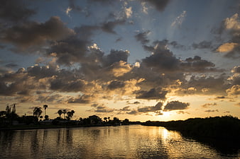 Dramatic sunset over river with clouds and palm trees