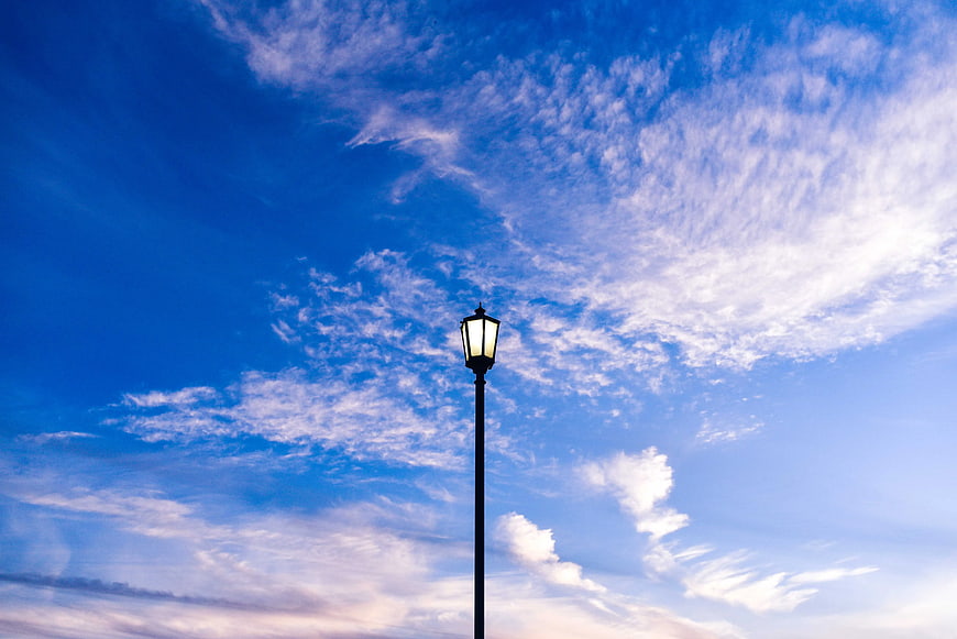 Illuminated Street Lamp Against Blue Sky with Clouds