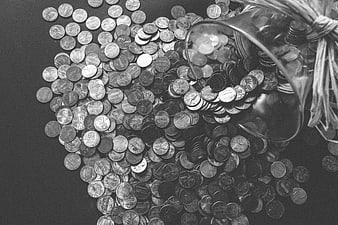 Grayscale photo of coins spilling from a glass jar