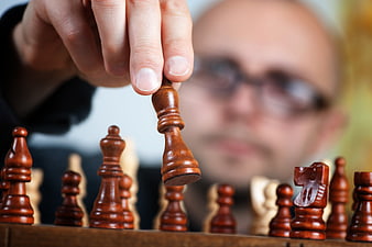Close-up of hand moving chess piece with blurred player