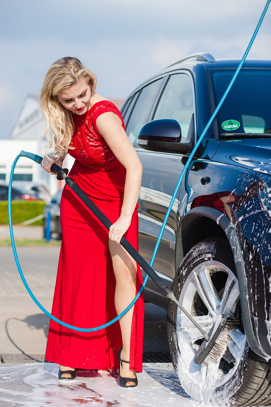 Woman in red dress washing car wheel with pressure washer
