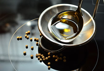 Olive oil in metal ladle with peppercorns on stovetop