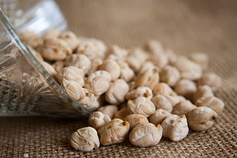 Dried chickpeas spilling from a glass jar onto a rustic burlap surface
