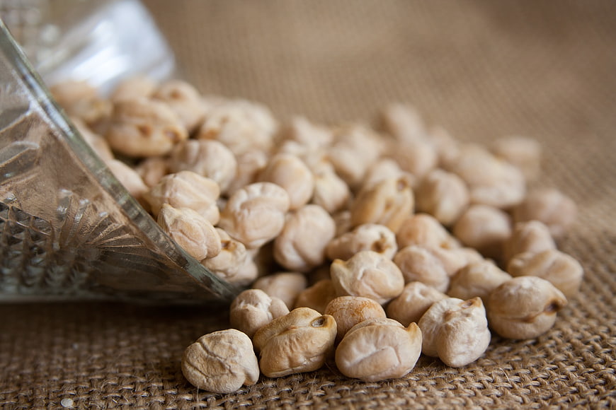 Dried chickpeas spilling from a glass jar onto a rustic burlap surface