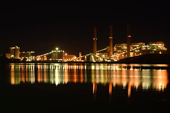 Illuminated industrial power plant at night with water reflections