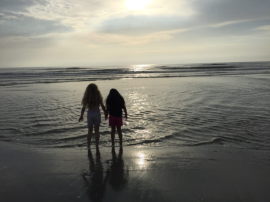 Two girls holding hands on beach at sunset