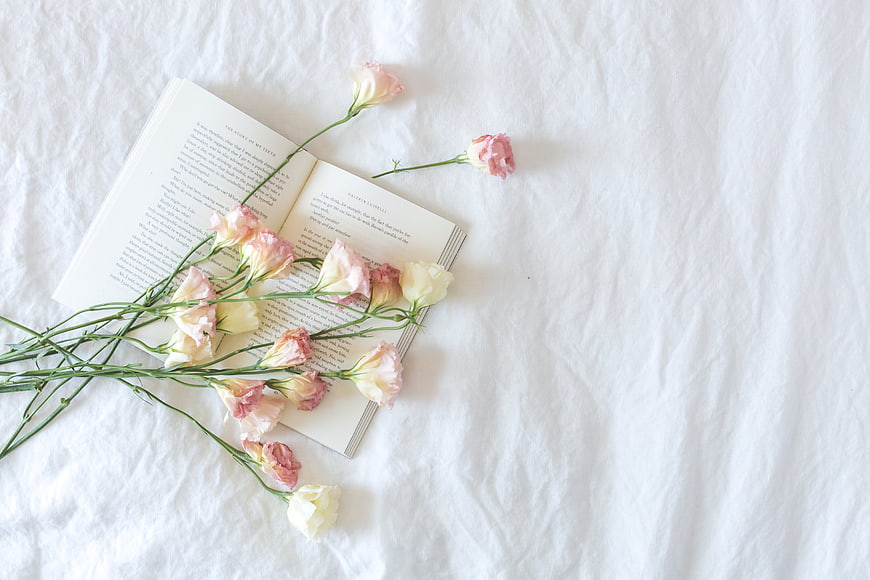 Flat lay of open book with pink and white flowers on white linen