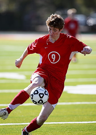 Young Male Soccer Player Kicking Ball on Green Field