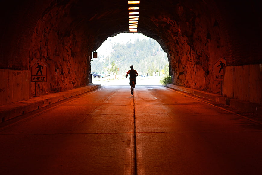 Silhouette of Man Running Through Dark Tunnel