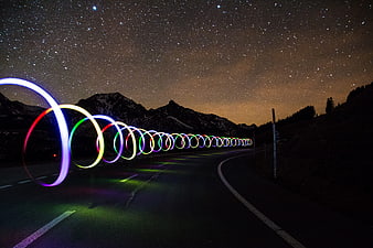 Colorful light painting circles on a mountain road under a starry night sky