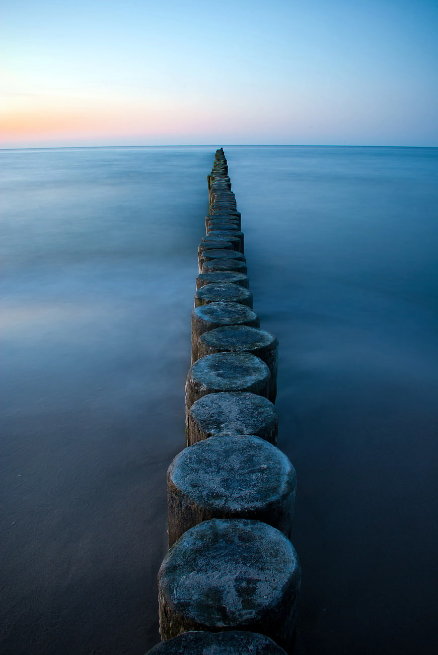 Long Exposure Wooden Groynes in Calm Sea at Sunset