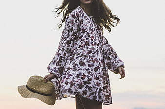Woman in Floral Dress Holding Straw Hat at Sunset