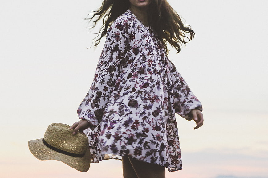 Woman in Floral Dress Holding Straw Hat at Sunset