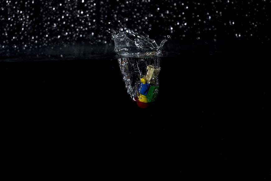 Colorful toy figure splashing into water against black background