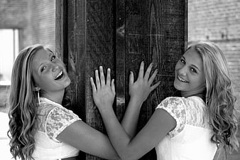 Two smiling young women leaning against a wooden post