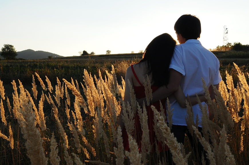 Couple embracing in tall grass field at sunset