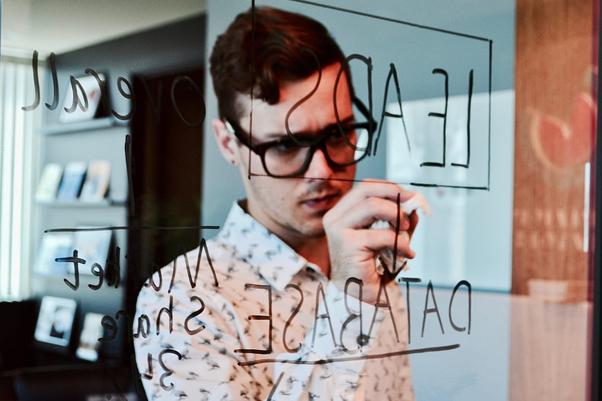 Businessman writing marketing strategy on glass whiteboard