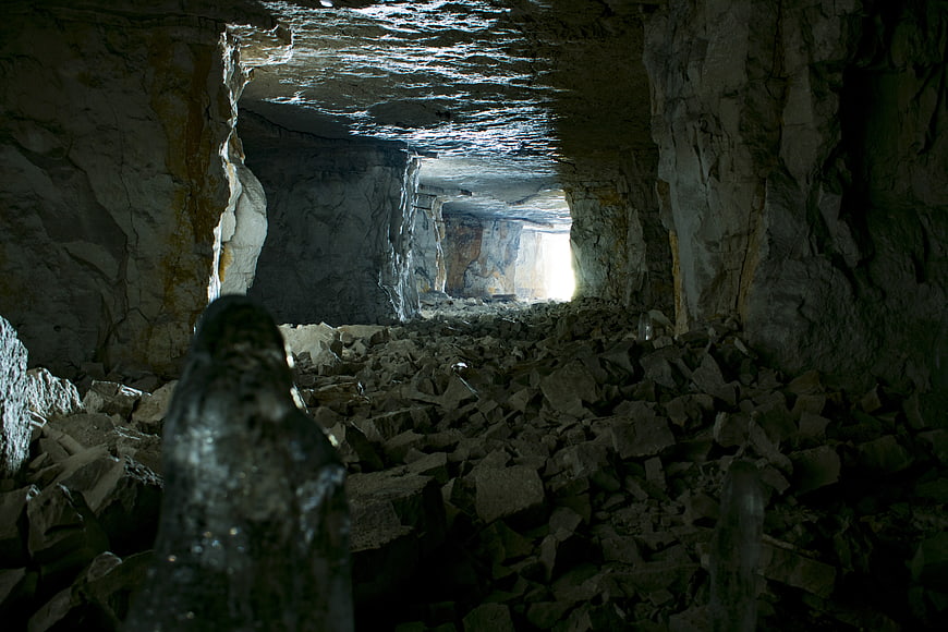 Dark Ice Cave Interior With Bright Exit And Rocky Debris