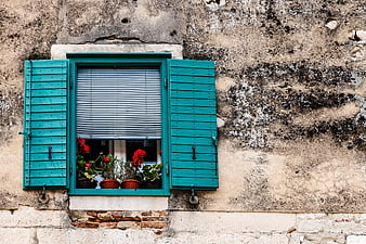 Turquoise shutters and red flowers on weathered stone wall
