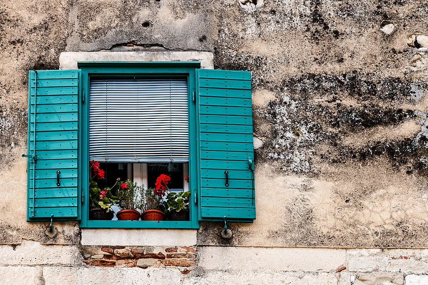Turquoise shutters and red flowers on weathered stone wall