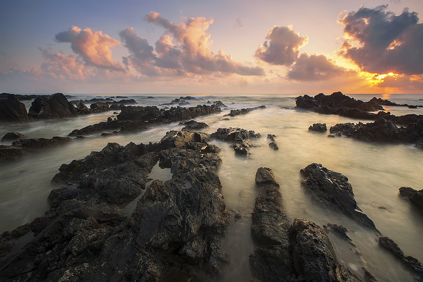 Dramatic Sunset Over Rocky Coastline with Misty Ocean Waves