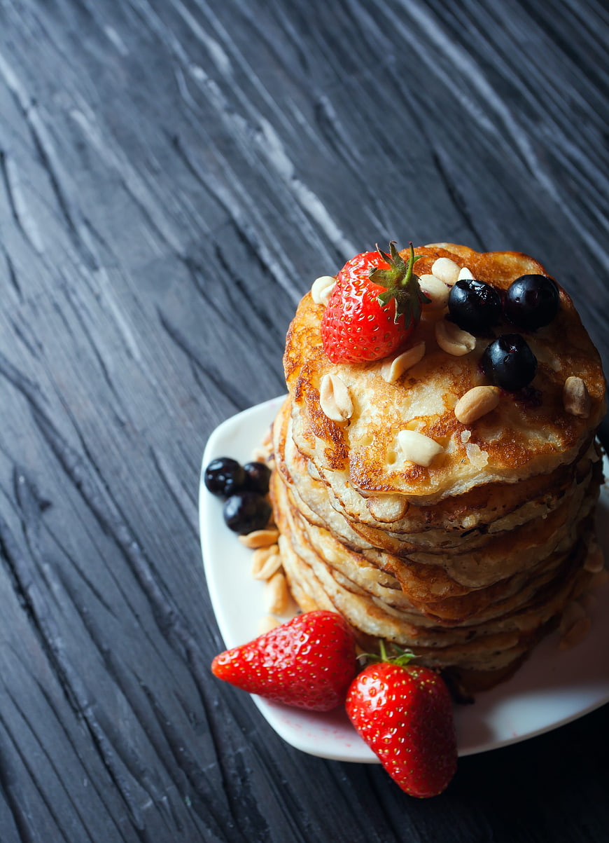 Stack of Golden Pancakes with Fresh Berries and Almonds on White Plate