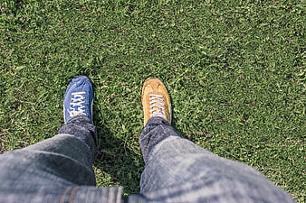 First-person view of mismatched blue and yellow sneakers on grass