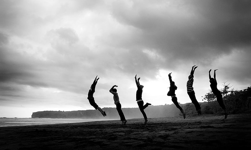 Silhouettes of people jumping on a beach against cloudy sky
