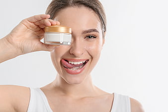 Happy woman holding skincare cream jar over eye