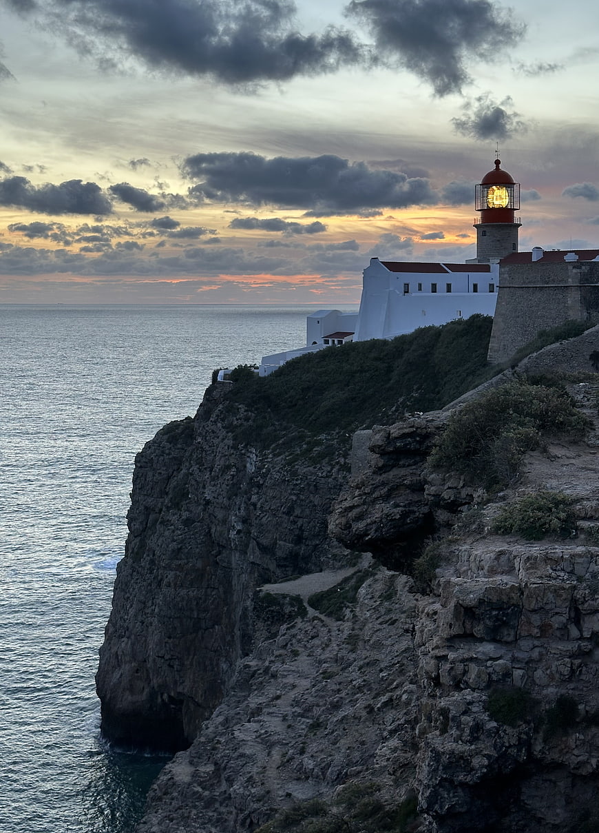 Illuminated Lighthouse on Rocky Cliff at Sunset