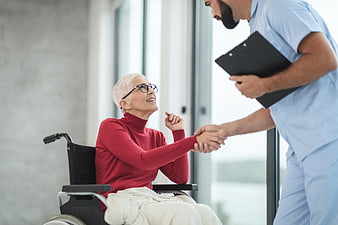 Senior woman in wheelchair shaking hands with male nurse