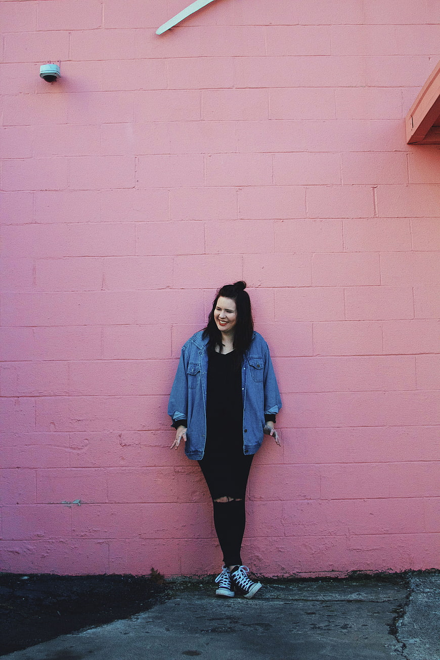 Happy woman in denim jacket standing against pink wall