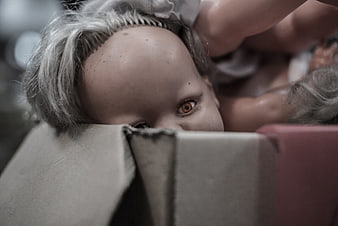Close-up of creepy doll peeking over cardboard box edge