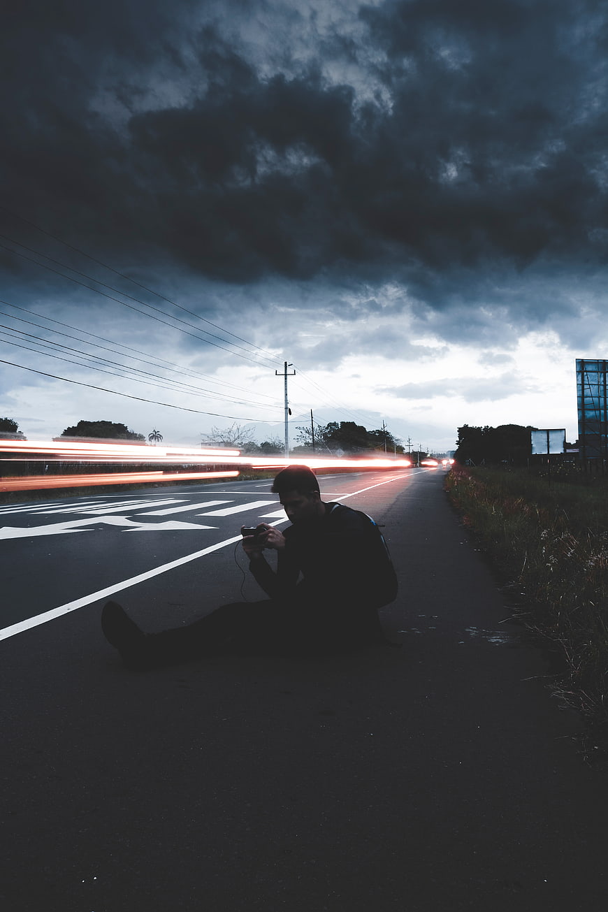 Man sitting on roadside with long exposure light trails