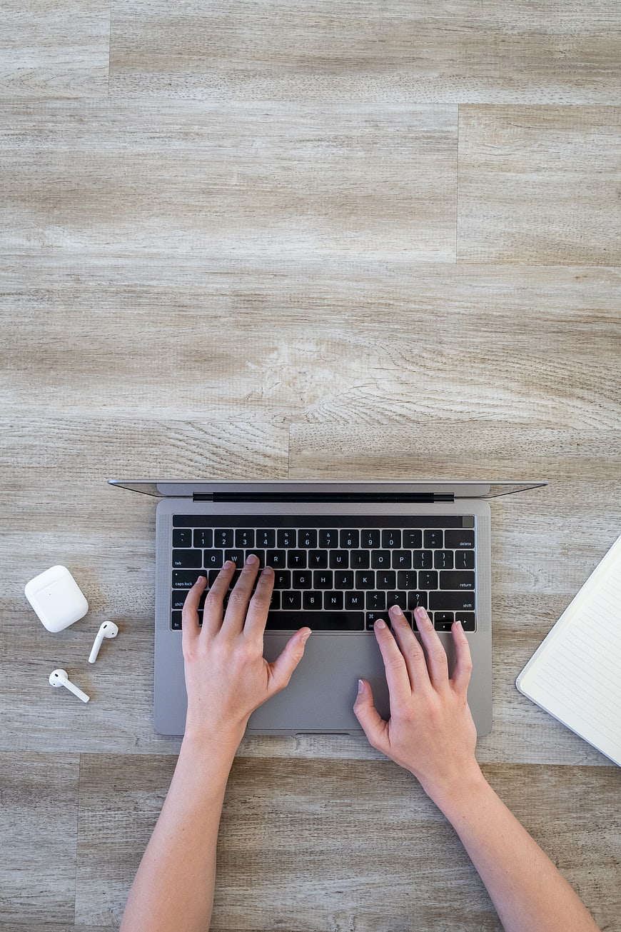Top View of Hands Typing on Laptop with Wireless Earbuds