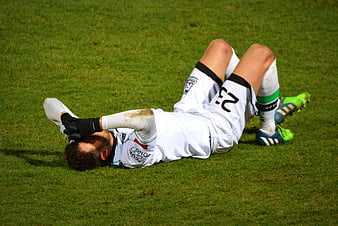 Injured soccer player lying on grass field in white uniform