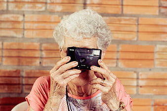 Senior woman holding vintage Kodak camera against brick wall