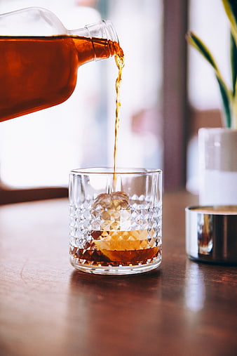 Pouring amber whiskey into a crystal glass with ice