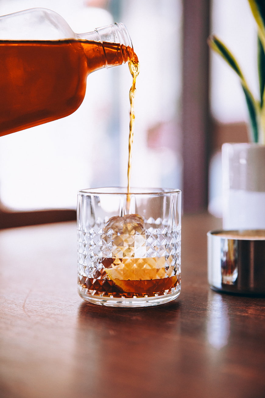 Pouring amber whiskey into a crystal glass with ice