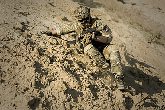 Soldier sliding down muddy hill with rifle