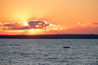 Dramatic Sunset Over Ocean with Silhouetted Boat and Clouds