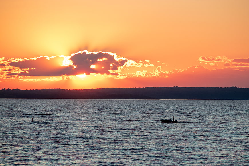 Dramatic Sunset Over Ocean with Silhouetted Boat and Clouds