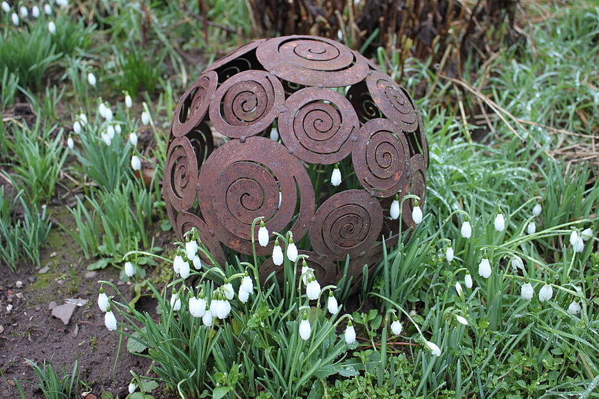 Rusty metal spiral sphere in snowdrop garden