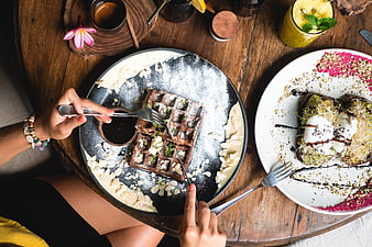 Top view of hands eating chocolate waffle and avocado toast at cafe